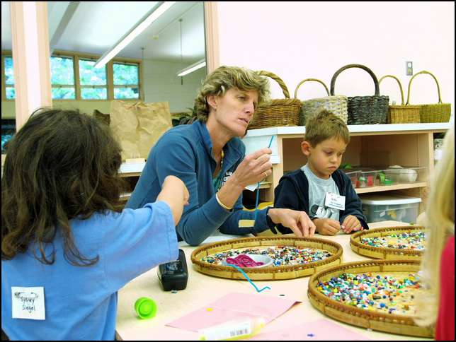 Teacher Peckie is demonstrating putting beads on colored 
