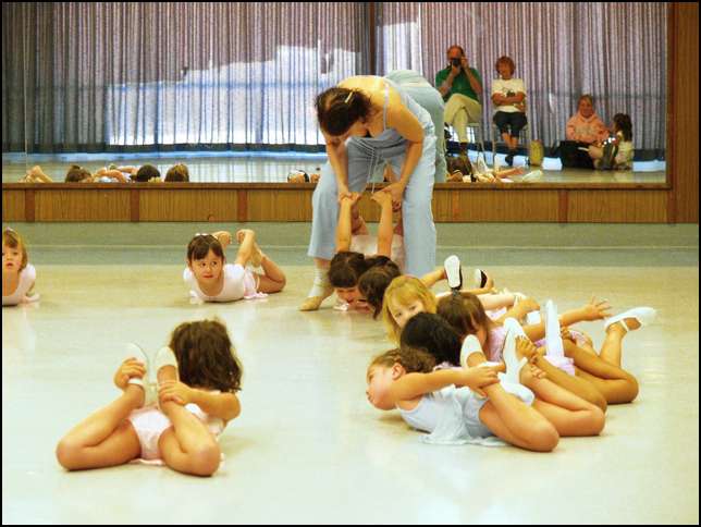 The teacher is picking Sydney up from the floor while she is holding on to her feet!